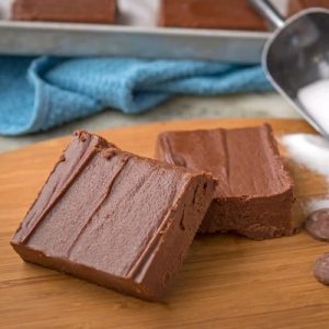 A thick block of creamy chocolate fudge sliced into generous squares on parchment paper